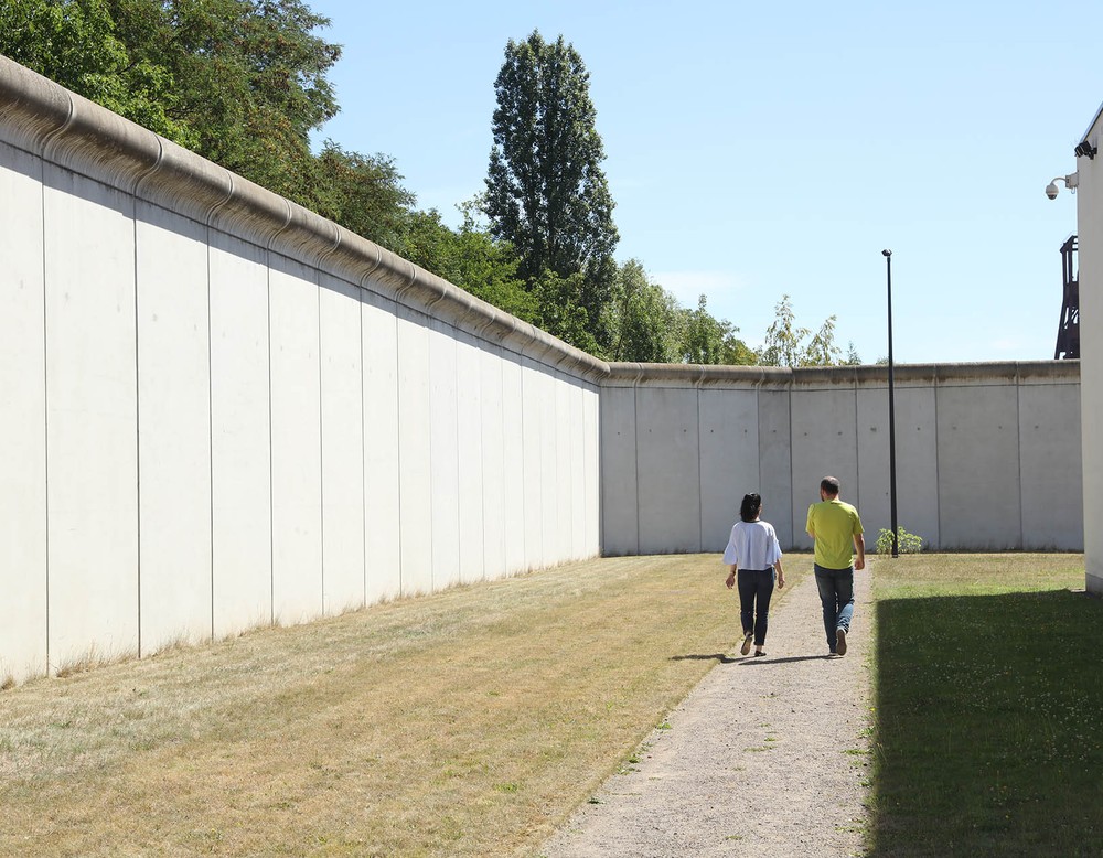 Ein Mann und eine Frau laufen weit entfernt auf einem Fußweg an einer Klinikmauer. (Bild: LWL/Wieland)